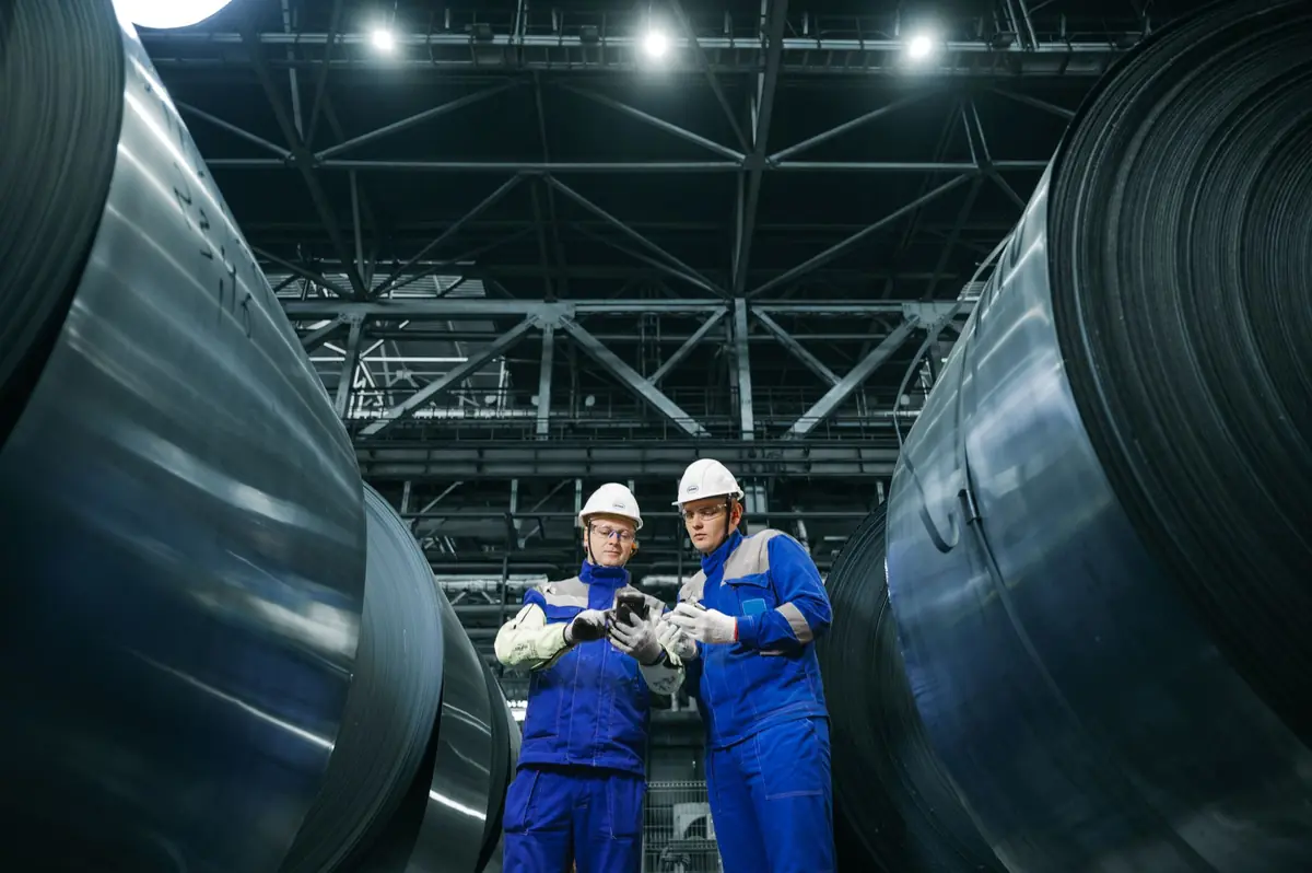 Workers inspecting large steel coils in a factory